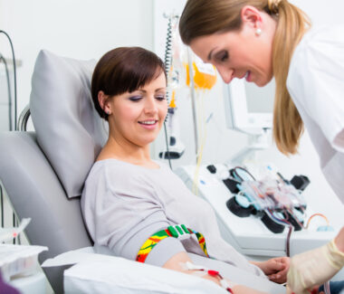 Female phlebotomist taking blood from a female blood donor reclining in a donation chair.